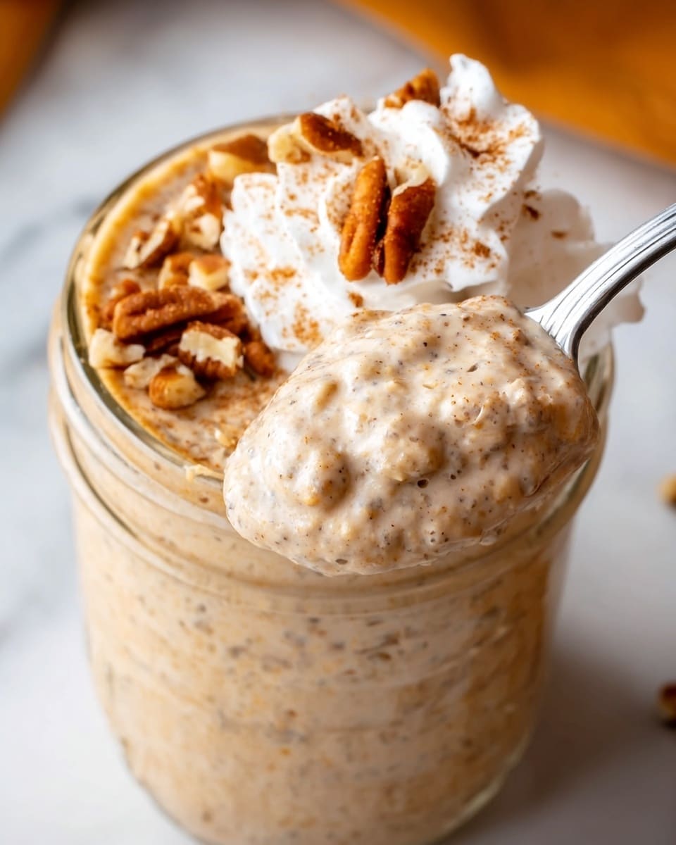 The image shows a close-up of a clear glass jar filled with a creamy, light brown pudding mixed with small bits of pecans. The pudding has a smooth texture with visible nut pieces throughout. On top, there is a dollop of white whipped cream sprinkled with a light dusting of cinnamon powder. A spoon, held by a woman's hand, is lifting a scoop of the pudding with pecans and whipped cream from the jar. The background is a white marbled texture with an out-of-focus orange element behind the jar. Photo taken with an iphone --ar 4:5 --v 7
