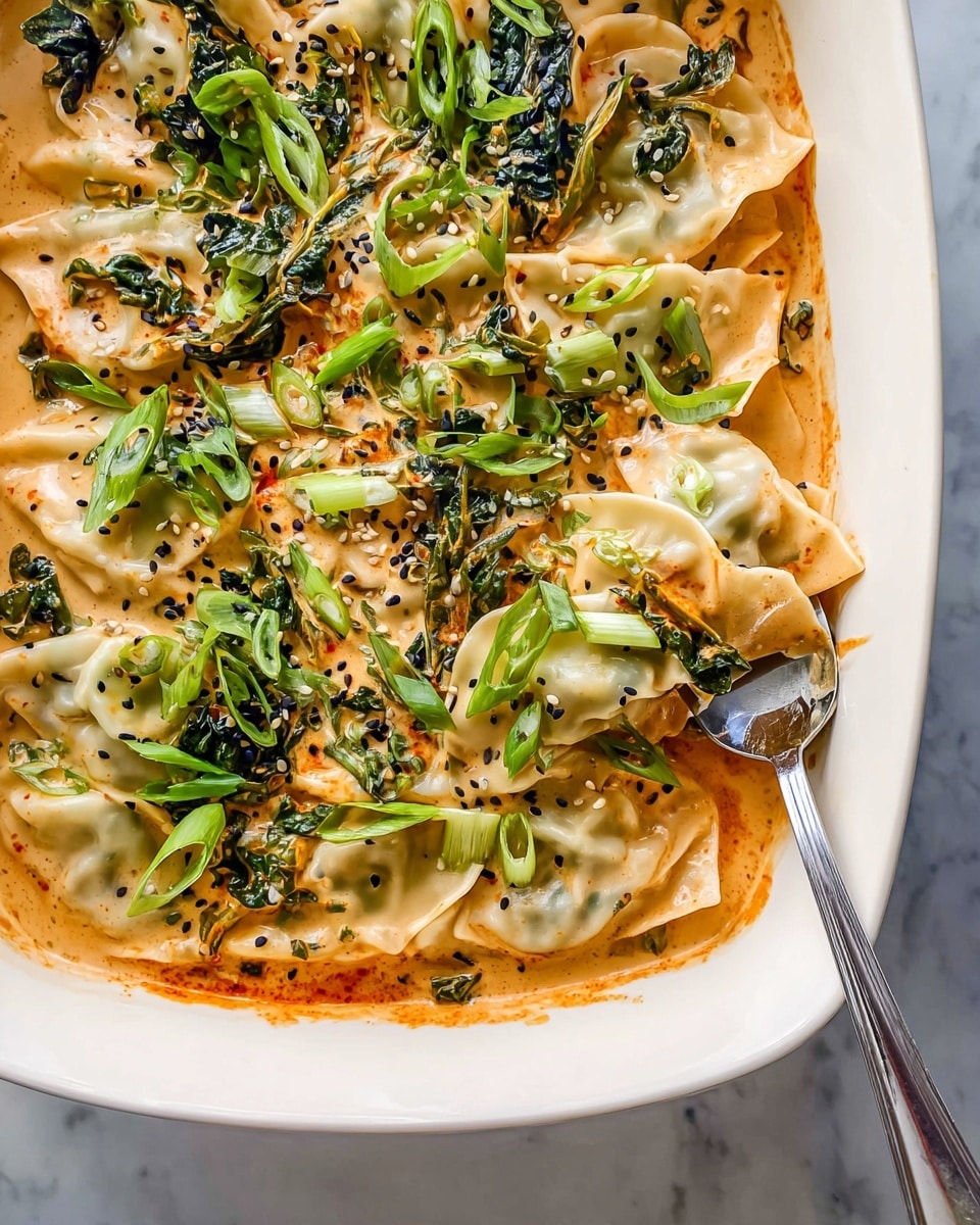The image shows a white dish filled with creamy orange sauce and several folded dumplings or pasta pieces layered throughout. The dumplings are soft with a light cream color and are partly covered in the sauce. Bright green chopped scallions and wilted leafy greens are sprinkled evenly on top, adding a fresh and vibrant contrast. Black sesame seeds are scattered over the dish, enhancing texture and color. A silver spoon is placed on the right side, lifting a dumpling from the sauce. The dish is placed on a white marbled surface photo taken with an iphone --ar 4:5 --v 7