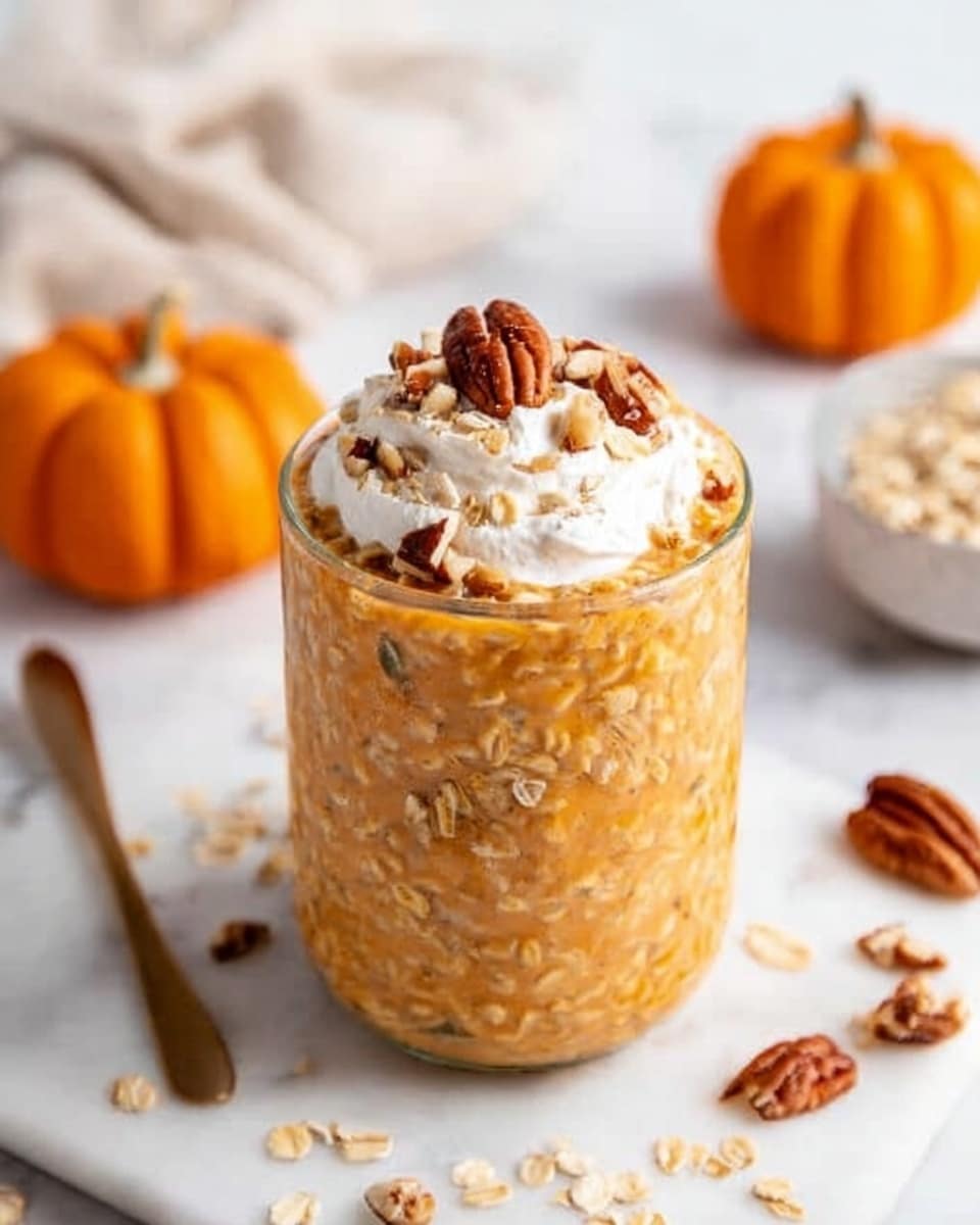 The image shows a glass jar filled with pumpkin oats, which have a creamy, orange color with bits of oats visible throughout. It is topped with a dollop of white whipped cream, a few whole pecans, and sprinkled chopped nuts. The jar is placed on a white marble surface with some scattered oats and nuts around it. In the background, there are two small orange pumpkins and a small white bowl with oats. The scene looks cozy and autumn-themed, photo taken with an iphone --ar 4:5 --v 7
