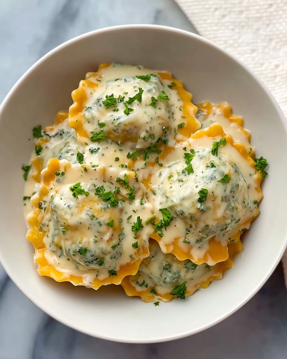 A white bowl holds four pieces of round ravioli layered side by side, each ravioli coated in a thick, creamy white sauce mixed with small green herbs that create a speckled texture. The ravioli themselves are golden orange with slightly ruffled edges visible beneath the sauce. On top, small green chopped parsley pieces are sprinkled unevenly across the dish. The bowl sits on a white marbled textured surface with a white cloth partially visible in the top right corner of the image. photo taken with an iphone --ar 4:5 --v 7