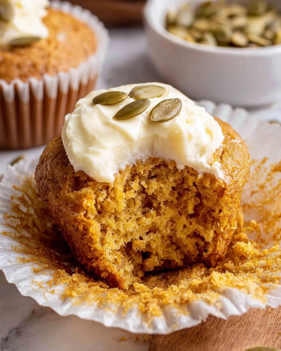 The image shows a muffin with a golden-brown crumb texture and a swirl of creamy white frosting on top, sprinkled with a few pumpkin seeds. The muffin is partially unwrapped, revealing a moist, slightly crumbly inside that contrasts with the smooth frosting. In the background, there is a white bowl filled with pumpkin seeds, all placed on a white marbled surface. The lighting highlights the muffin’s soft texture and the creamy frosting detail. photo taken with an iphone --ar 4:5 --v 7