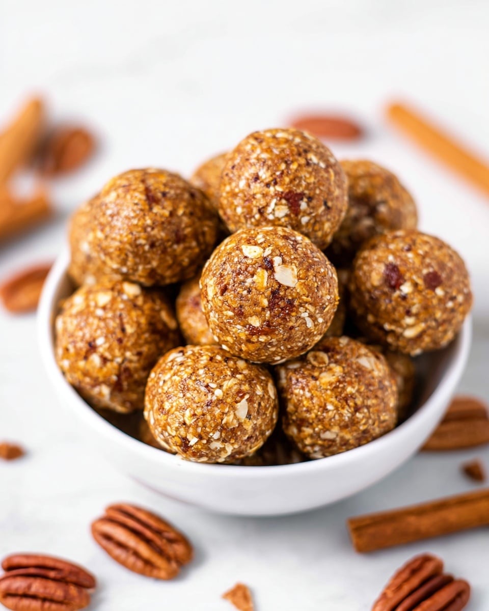 A white bowl filled with round, golden-brown energy balls that have a rough texture with bits of oats and nuts visible. Around the bowl and mixed in are whole pecan nuts adding a darker brown contrast. The background is a white marbled texture scattered with cinnamon sticks and pecan nuts, creating a warm and cozy feel. The focus is sharp on the top energy ball, showing its detailed texture, while the rest softly blur into the background. photo taken with an iphone --ar 4:5 --v 7