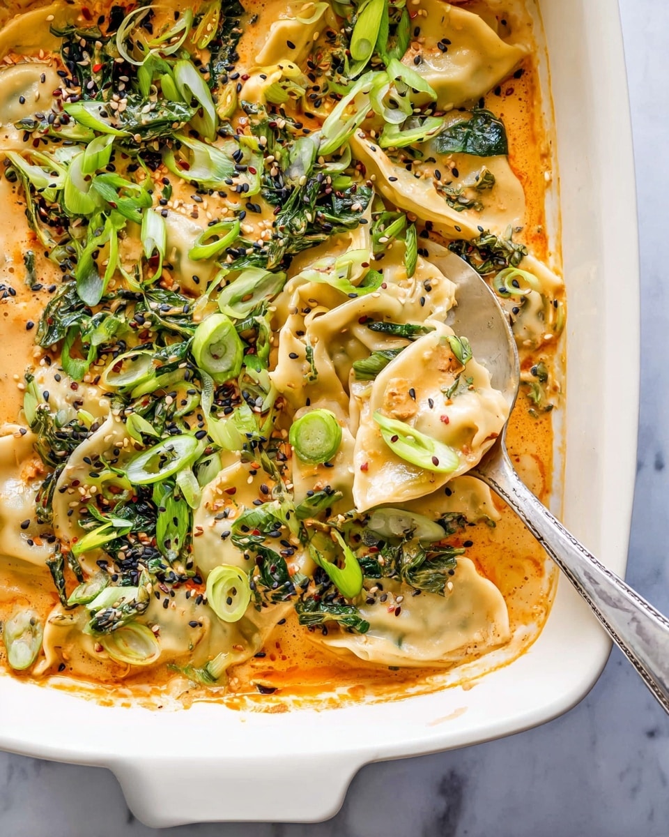 A white baking dish filled with a creamy orange sauce layered with dumplings that are soft and slightly browned on top. The dumplings are folded and partially hidden under the sauce, which looks thick and smooth. On top, there are chopped green herbs and green onions scattered evenly, along with some black sesame seeds and small hints of chili flakes. A silver spoon is partly lifting one dumpling from the sauce, showing its soft texture. The dish sits on a white marbled textured surface. Photo taken with an iphone --ar 4:5 --v 7