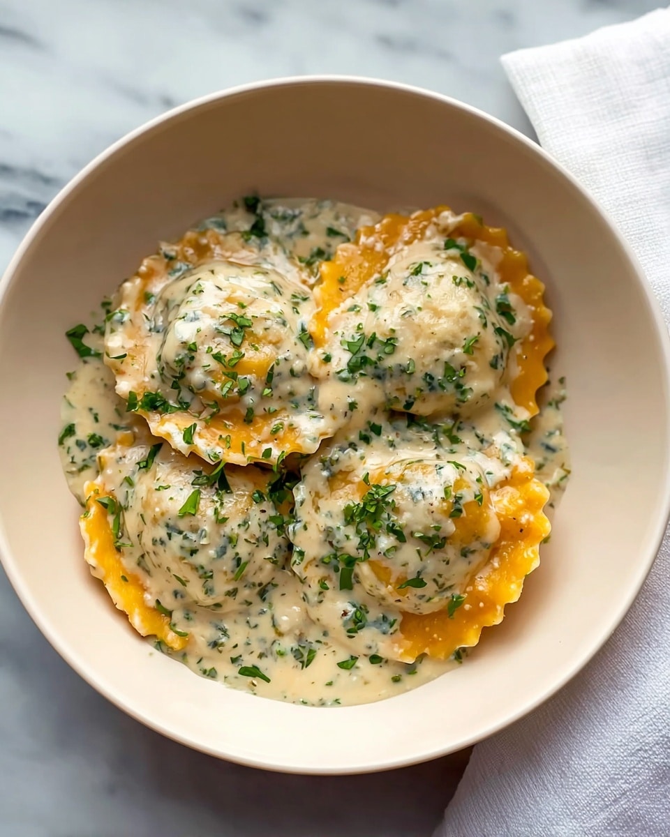 A close-up view of four round ravioli pieces arranged inside a white bowl with a light blue interior, each piece covered in a creamy white sauce mixed with green herbs. The ravioli pasta is orange in color with scalloped edges lightly visible beneath the sauce. Small chopped fresh green herbs are sprinkled over the top, adding a touch of color contrast. The bowl is set on a white marbled textured surface, with part of a white cloth napkin showing at the top right corner. photo taken with an iphone --ar 4:5 --v 7