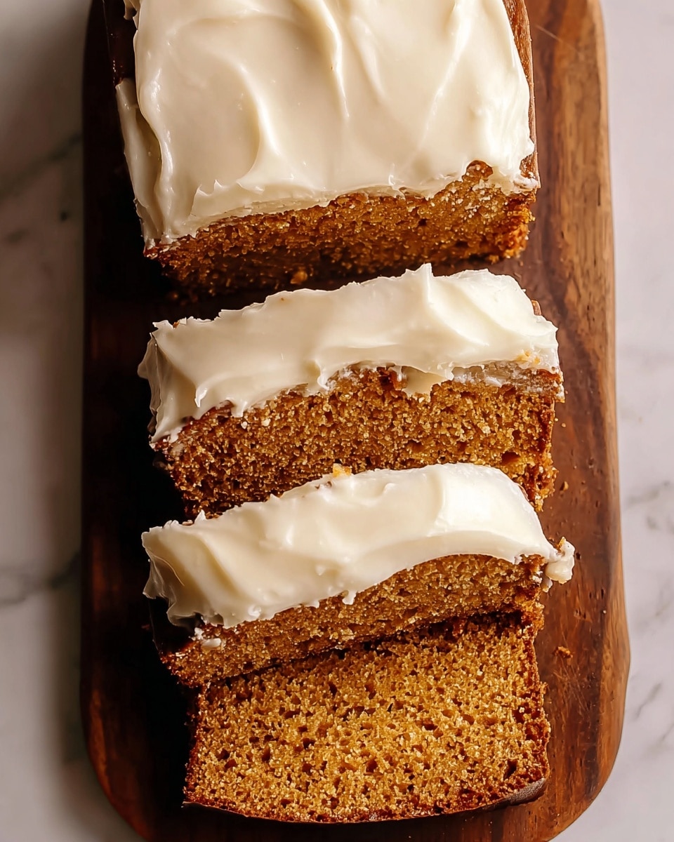 A sliced loaf cake is shown from above, with three slices visible, each topped with a thick, creamy, white frosting layer. The cake itself is a warm brown color with a moist and slightly crumbly texture. The frosting is smooth but has some soft, uneven edges that give it a homemade feel. The cake rests on a dark wooden board which contrasts softly against the white marbled surface underneath. Photo taken with an iphone --ar 4:5 --v 7