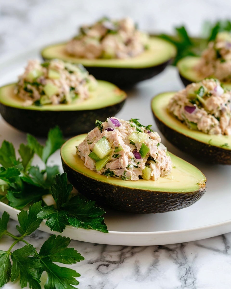 The image shows six avocado halves arranged on a large white plate placed on a white marbled surface. Each avocado half is filled with a creamy mixture that has a light beige color with visible chunks of purple onion and green celery pieces, sprinkled with chopped fresh herbs and small black pepper bits on top. The dark green avocado skin edges contrast with the smooth pale green flesh holding the filling. A small white bowl with cracked black pepper is near the plate, with stacked white plates and vintage silver forks at the background right. A white napkin is placed partially on the table near the bottom right of the plate. photo taken with an iphone --ar 4:5 --v 7
