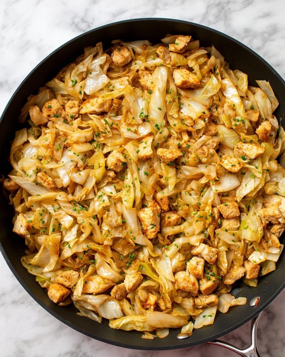 A black pan filled with a cooked mix of sliced cabbage and chicken pieces. The cabbage is soft and lightly browned, showing pale yellow and light brown tones with some parts slightly crispy. The chicken chunks are small, cooked to a golden color with a tender texture. The dish has tiny green herb bits sprinkled on top, adding a fresh note. The pan is placed on a white marbled surface, with the food spread evenly inside the pan. photo taken with an iphone --ar 4:5 --v 7