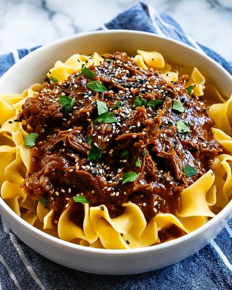 A white bowl filled with wide, flat yellow pasta noodles at the base, topped with a generous portion of shredded brown meat covered in a thick, rich brown sauce. Small green herb leaves are scattered on top, along with black and white sesame seeds adding texture. The bowl rests on a blue cloth with white stripes, set against a white marbled surface. photo taken with an iphone --ar 4:5 --v 7