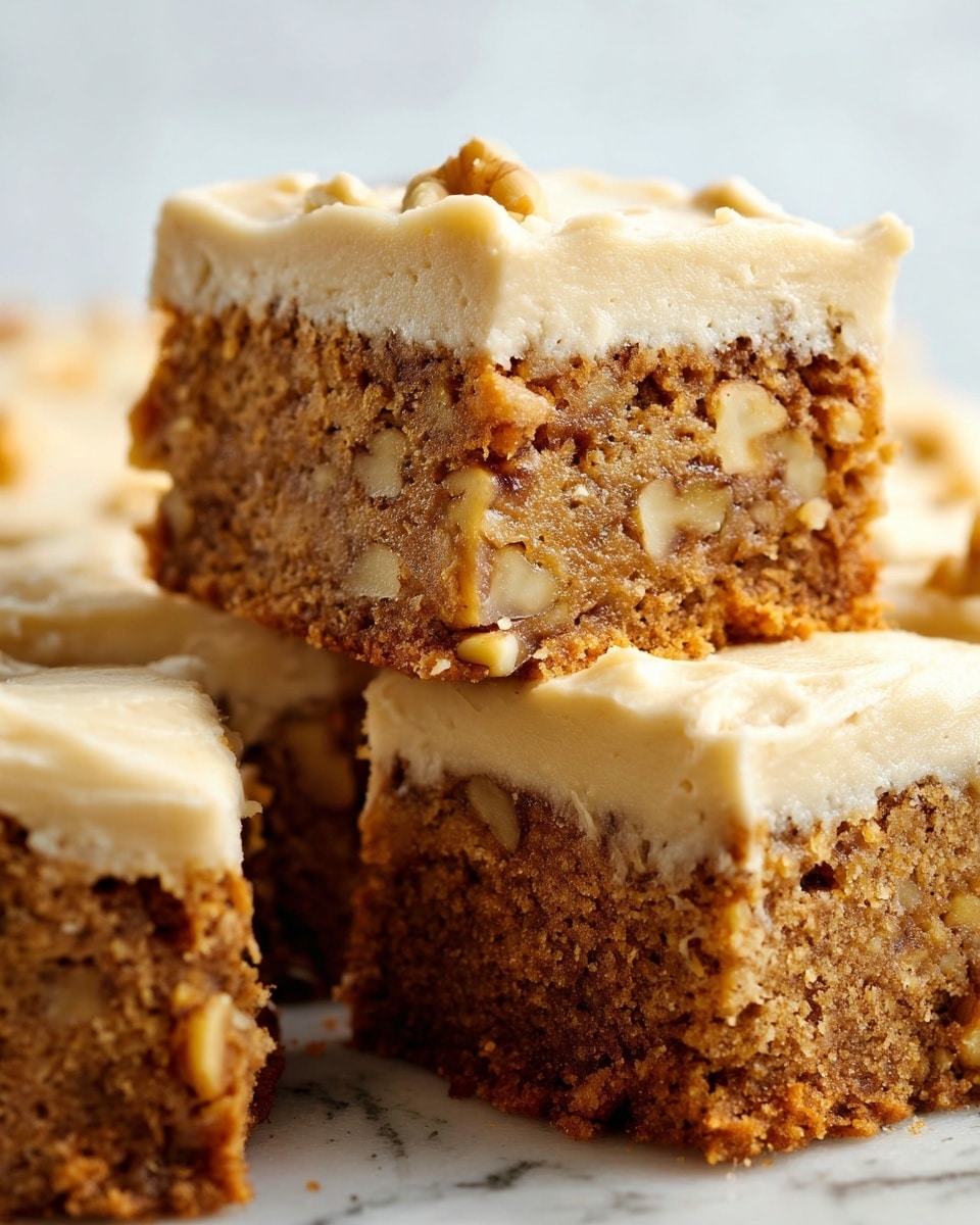 A close-up view of three square cake pieces stacked on a white marbled surface, each with two layers: the bottom layer is a dense, moist brown cake with visible nuts embedded inside, showing a crumbly texture, and the top layer is a thick, creamy light beige frosting with a smooth yet slightly textured surface. The top cake piece is placed slightly at an angle, resting on the middle piece, revealing the dense nutty texture inside. The background is softly blurred to keep focus on the cake pieces. photo taken with an iphone --ar 4:5 --v 7