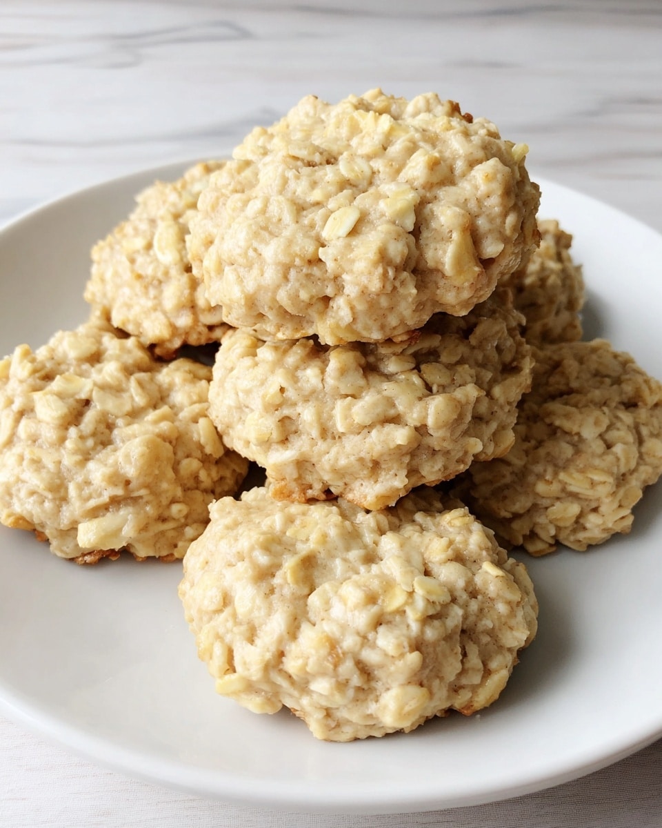 A white round plate holds a stack of six oatmeal cookies, each thick and rough-textured with a pale creamy beige color. The cookies are uneven in shape, with visible oats giving them a chunky look. The plate is set on a white marbled surface that adds a clean, bright background to the overall natural, homemade appearance of the cookies. photo taken with an iphone --ar 4:5 --v 7