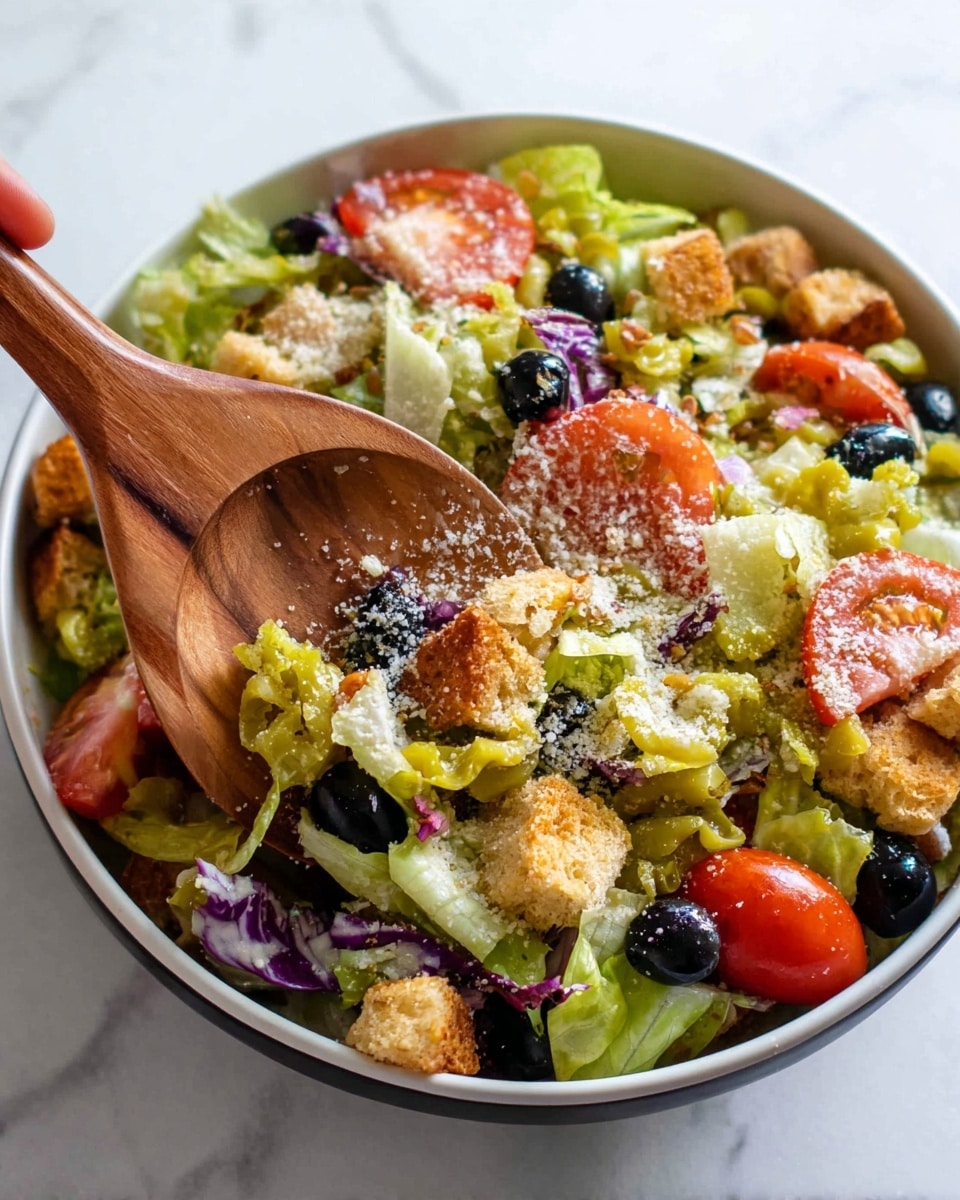 A white bowl filled with a mixed salad showing clear layers: the bottom layer is a bed of chopped green and purple lettuce with a fresh texture, the middle layer consists of scattered bright yellow pepperoncini, crunchy light brown croutons, and shiny black olives, and the top layer showcases slices of red tomatoes with a juicy and soft texture, all sprinkled with a dusting of finely grated white cheese. The salad is being tossed with a wooden spoon that is partially visible inside the bowl, held by a woman's hand. The setting is on a white marbled surface. photo taken with an iphone --ar 4:5 --v 7