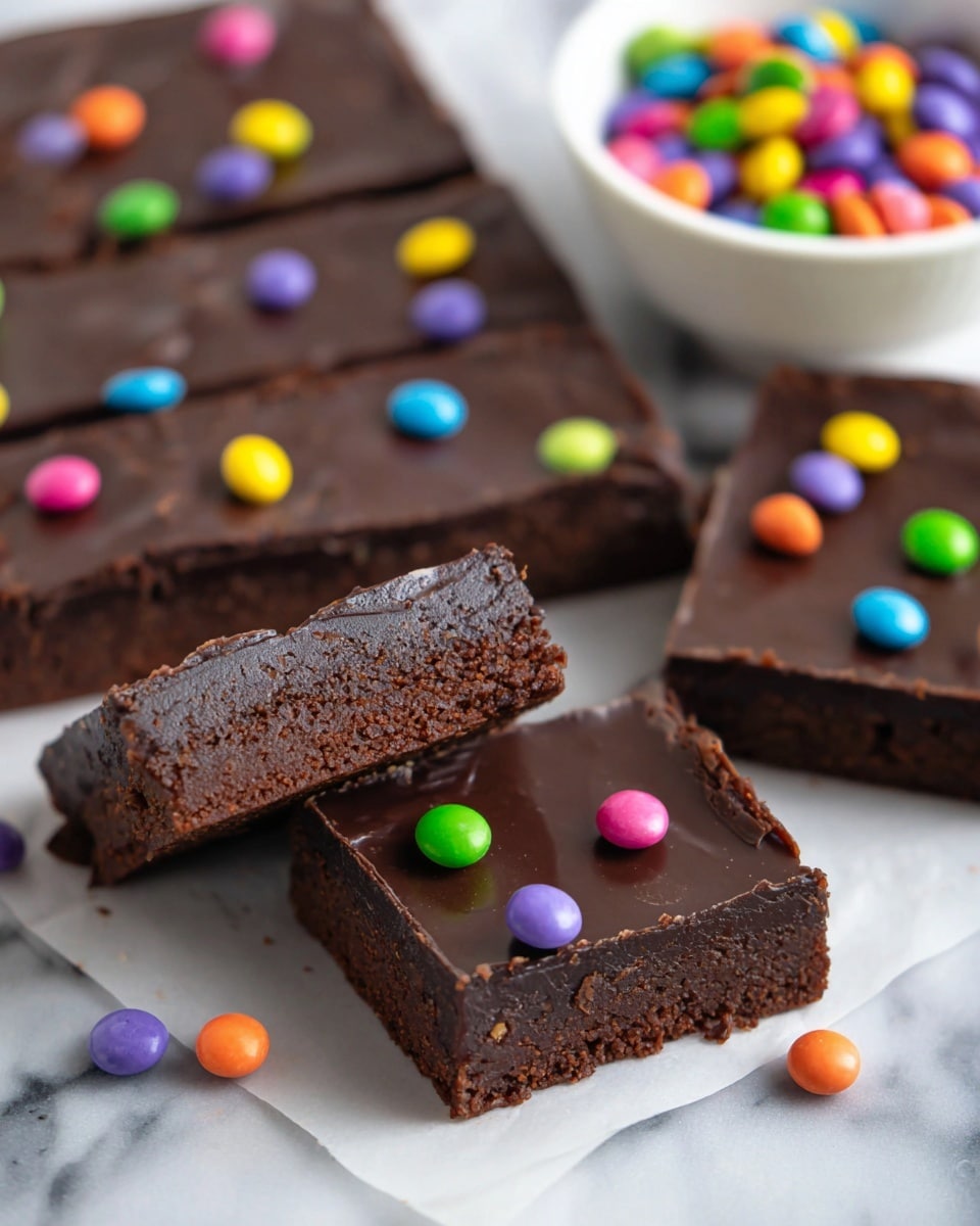 The image shows several rectangular chocolate brownies laid out on a white marbled surface. Each brownie has two layers: a thick, dense, dark brown base with a slightly crumbly texture and a smooth, glossy chocolate topping layer. On top of the chocolate layer, there are small, round, colorful candy balls scattered in shades of purple, green, orange, yellow, pink, and blue. One brownie piece is lifted up, showing the rich, dark brown inside clearly. In the background, there is a white bowl filled with the same colorful candy balls. Photo taken with an iphone --ar 4:5 --v 7