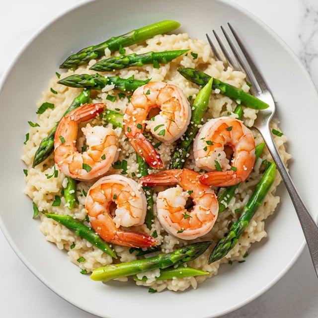 A shallow white bowl holds creamy risotto with a soft, slightly shiny texture as the base layer. Scattered within the risotto are bright green asparagus pieces, slightly tender and crisp, adding color and texture. On top, there are five pink-orange cooked shrimp, slightly curled with a firm texture. The dish is sprinkled with finely chopped green herbs and a light dusting of grated cheese, adding small pops of texture and color on the surface. A silver fork rests on the side of the bowl, and the background shows a white marbled texture. photo taken with an iphone --ar 4:5 --v 7